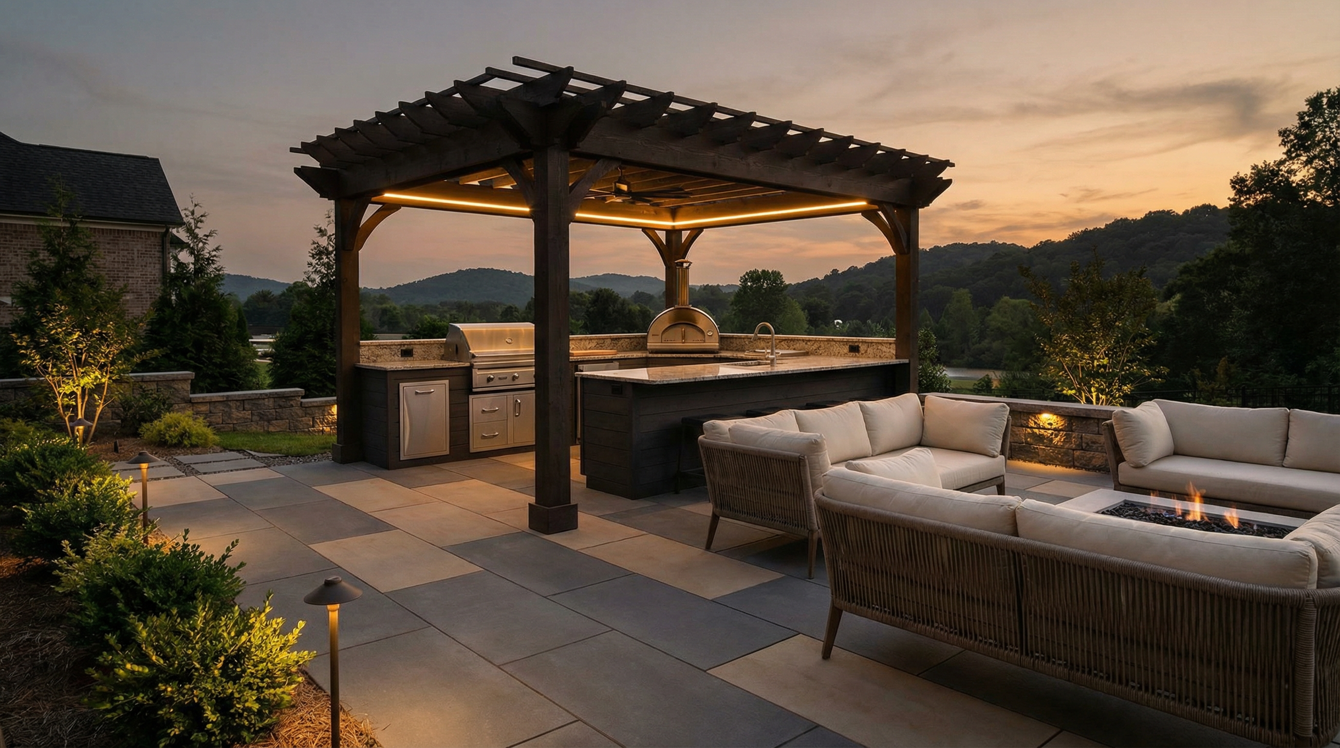 Upscale outdoor kitchen with built-in grill, pergola, and fire pit lounge on large-format pavers at dusk in Upstate South Carolina