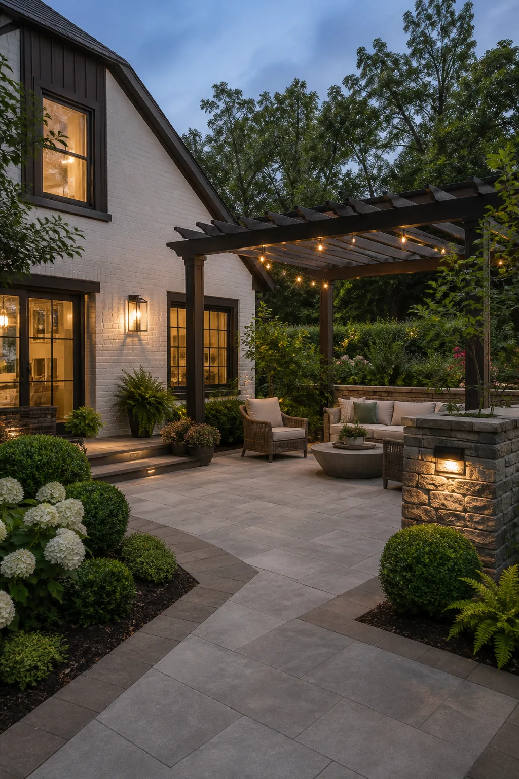 Warm gray and taupe paver patio coordinated with a white brick home, dark trim, pergola, and green landscaping